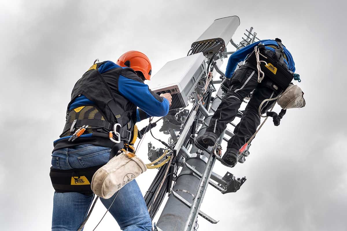 Zwei Mitarbeiter des Unternehmens Axians installieren am 5. April 2019 im Kanton Genf eine 5G-Antenne für die Mobilkommunikation auf einem Mast auf dem Dach eines Gebäudes im Viertel La Gradelle in Chene-Bougeries.  Foto: Keystone-SDA / Martial Trezzini  