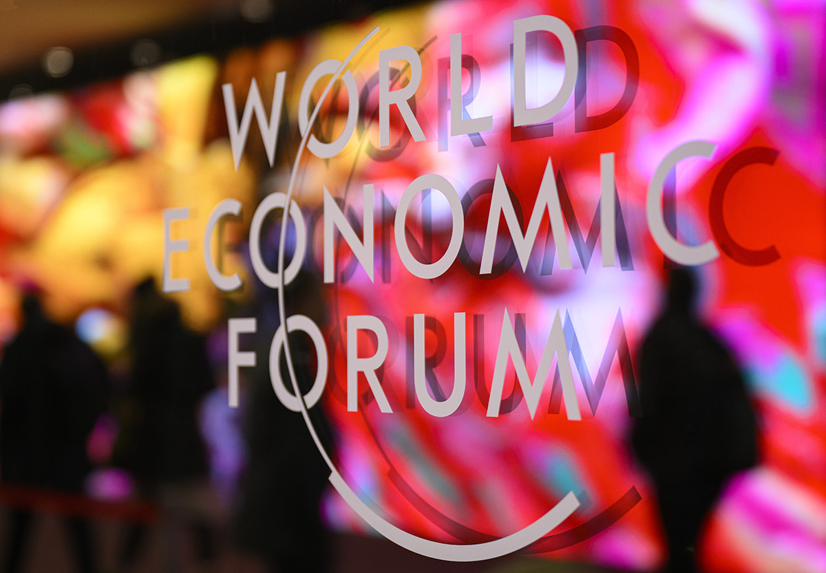 Das Logo des WEF ist auf einem Fenster des Kongresszentrums abgebildet, während sich Teilnehmer und ein von künstlicher Intelligenz generiertes Kunstwerk des türkisch-amerikanischen Medienkünstlers Refik Anadol im Kongresszentrum am 14. Januar 2024, am Vorabend des 54. jährlichen Treffens des Weltwirtschaftsforums (WEF) in Davos, spiegeln. Das diesjährige Weltwirtschaftsforum steht unter dem Motto «Rebuilding Trust» (Vertrauen wieder aufbauen).  Foto: Keystone-SDA / Laurent Gilliéron