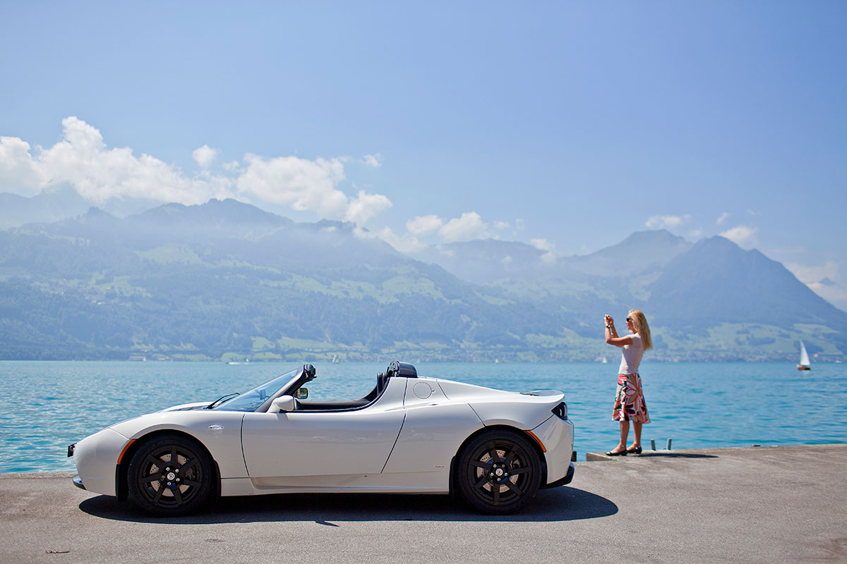 Eine Frau fotografiert am 19. Juli 2010 am Ufer des Vierwaldstättersees in Gersau. Sie ist mit einem «Tesla Roadster Sport» unterwegs. Elektroautos weisen über ihre gesamte Lebensdauer hinweg eine bessere Umweltbilanz auf als Fahrzeuge mit Verbrennungsmotor. Foto: Keystone-SDA/Gaëtan Bally